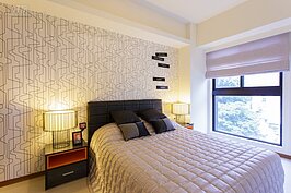 人有三分之一的時間都是躺在床上睡眠，因此對於臥室舒適與否就顯得格外重要。中等價位的雙人床加上邊桌，所花費的價格並不會很貴。以這次示範的主臥室裝潢，簡約中帶點新潮，最主要是床頭後方牆壁不以油漆為塗料，而是選擇幾何線條的壁紙，營造出特別的氛圍。
不過頭頂上有梁，這是許多人較為避諱的地方，可以在床頭加上一組床頭櫃以增加與牆壁之間的距離，就可避開樑壓頂的困擾。