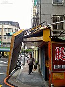 店家招牌倒下，民眾從下方走過，景象十分危險。