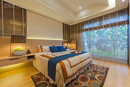 主臥室除了有一大片對外窗外，在床頭部分也有左右兩片小窗。窗簾不採用時下流行的布質窗簾，而是採用木片百葉窗，呼應中國風木質溫暖的設計主軸。
燈光部分，設計師略降低天花板高度以容納LED嵌燈，床頭與邊桌則採用間接照明，讓夜間的燈光不會這麼的直接刺眼。