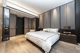 接續著客廳與長廊的中式設計概念，主臥室內木紋地板與床頭木質左右邊桌，讓臥室充滿了溫暖的氛圍。床頭後方的布面滑門櫃與左方衣櫥採同色系同質料設計，整體感覺就是簡單但不失質感。