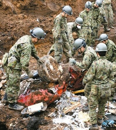 日本自衛隊十八日在熊本縣南阿蘇村山崩地點檢視一輛剛挖出的汽車殘骸。 美聯社
