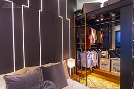 大約四坪左右的臥室，若立了一組有門的木頭衣櫥，除了會縮顯空間感，而且也無法強調主人品味。因此設計師大膽採用開放空間的上下兩層衣帽間設計，下層所有衣物都是對外開放；上層則可收納大型物品，例如遊歷諸國用的行李箱。
當然想要保有一點隱私權，例如朋友到訪的話，則可外掛布幔遮掩。
最引人注目的莫過於床頭牆壁上如同紐約高聳摩天大樓的意象景致，這是利用LED燈條搭配不同轉折所營造出來的氣氛。