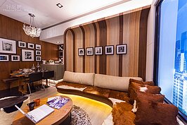 高聳直達天花板的夾板沙發牆壁，是這個設計案中最為顯眼地方。木頭所營造出來的上下直線線條，如同紐約都會中一幢幢高聳的摩天大廈。
沙發為現地木作所製作，不使用外面成品，目的就是與背牆相呼應。軟墊使用仿皮草的棕白紋路材質，讓客廳空間充滿了溫馨的氛圍。