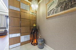 一進入玄關，就被牆上的頗有來頭的國畫吸引，一旁角落放著象徵財富的彌勒佛與可淨化身心靈的鹽燈，讓玄關整體氣氛豐富又不雜亂。更引人注目的就是在彌勒佛後方的木板與拉絲毛玻璃所組成的牆面，整體感覺則是沈穩中帶著些許活潑氣息。