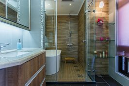 主臥室盥洗檯面採不怕水又耐磨的人造石，色彩則與內側浴缸相呼應。在盥洗的浴室內牆面則是採用深色木紋石，可營造出溫暖的感覺。