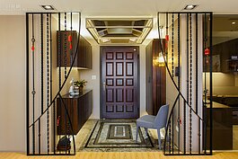 玄關的設計最吸睛的地方莫過於兩邊如同拉開窗簾般的鑄鐵窗花欄杆，雖然看似冷冽卻又有帶著視角開展的一個感覺。設計師強調這樣的做法還有與客廳做出區隔的用意。
地面的石材拼貼地板與玄關天花板燈具相呼應，遠遠看過去就彷彿置身在藝術展區中那樣的精緻典雅。