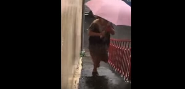 婦人想要撐雨傘外出；但雨傘馬上被冰雹砸出1個洞，只好趕緊躲回屋簷底下。圖／翻攝爆料公社
