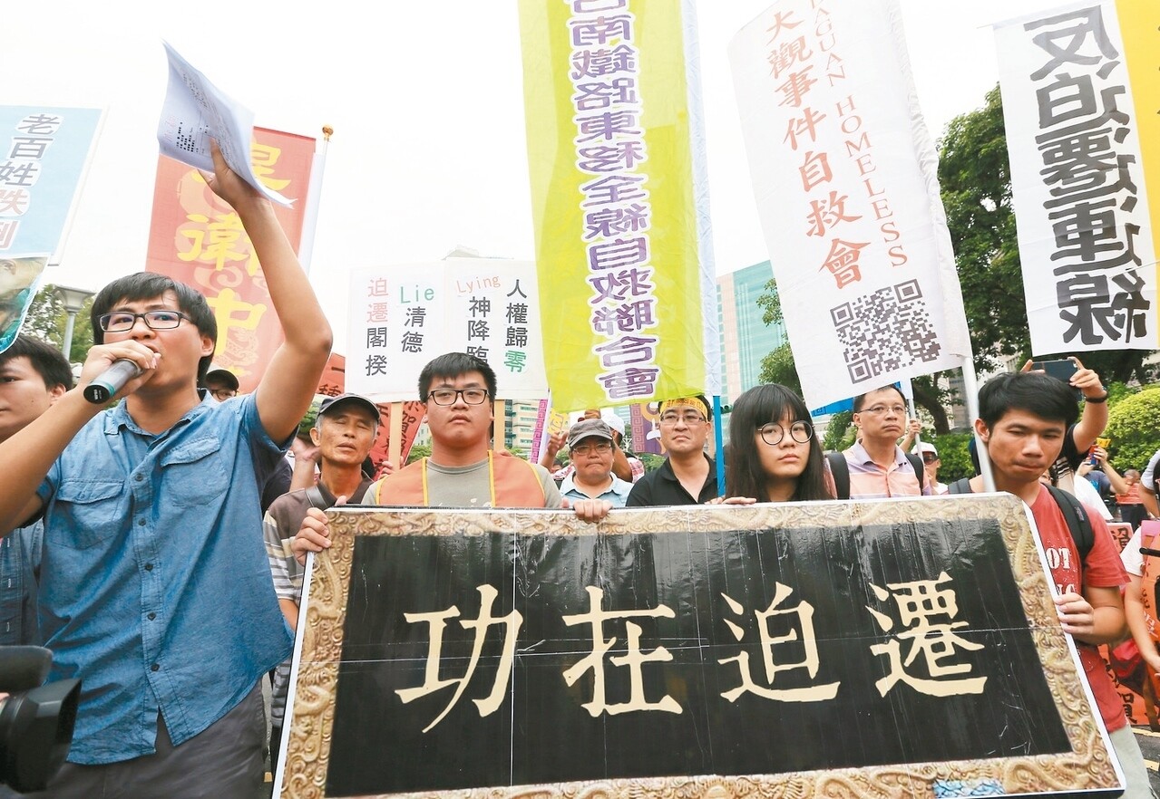 反南鐵東移自救會成員到行政院前抗議，並自製「功在迫遷」匾額，希望能親手交給賴清德，隨後和警察發生推擠衝突。後來警方讓抗議民眾將「功在迫遷」匾額貼在大門上才結束抗議。 記者陳柏亨／攝影