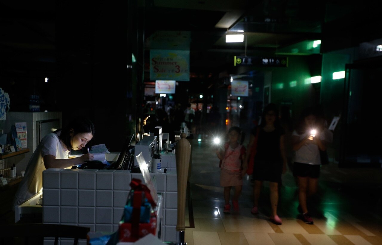 大潭電廠跳機造成全台昨天下午以後大停電，台北京站時尚廣場傍晚後也整個停電，櫃姐們用手機微弱的光線算帳，一旁的媽媽帶著女兒用手機來照亮道路。 記者鄭超文／攝影