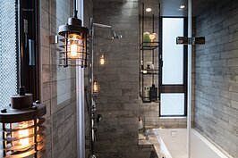 浴室牆面部分則是特意選擇陳舊斑駁感的磁磚，讓整體氛圍有種希臘風格，不過因為會太過於陰柔，因此設計師特別加入兩組垂吊的鐵製吊燈以及鐵件吊櫃，讓浴室空間增添些硬派感覺做調和。