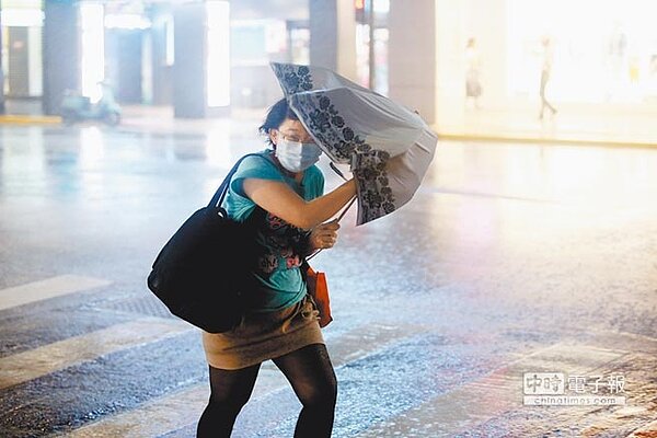 台北地區晚間出現間歇性風雨,刮起的強風,讓民眾只能用傘抵著風前進。(陳信翰攝)