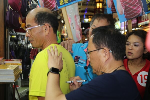 國民黨台北長候選人今晚到萬華區艋舺夜市拜票，有支持者要求在背上簽名。記者魏莨伊／攝影 