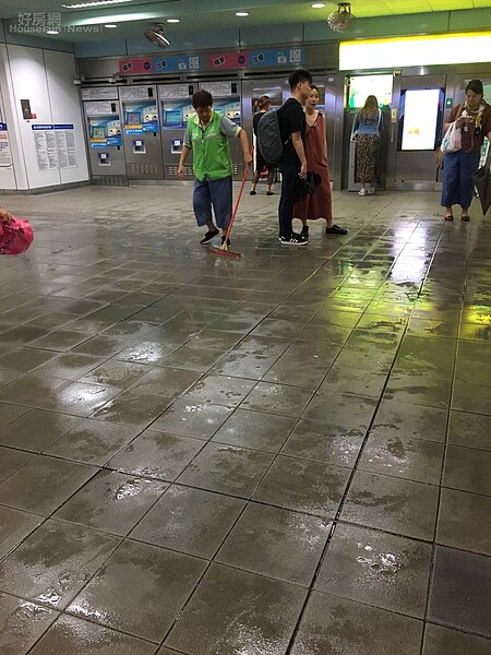 由於雨勢猛烈打進捷運大安站大廳,清潔人員正在努力掃水。(好房網News記者楊欽亮攝影)