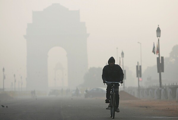 印度空氣汙染嚴重，一名男子在首都新德里國王大道騎自行車，後方的獨立紀念碑「印度門」在霧霾中形影模糊。（路透）