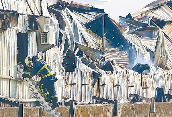 台中市大雅區中和六路一處鐵皮工廠3日凌晨大火,2名消防人員進入救災時遭倒塌的鋼骨壓身而殉職,圖中消防員爬梯進入火場,身後的廠房歪七扭八,突顯合法工廠的重要。(黃國峰攝)