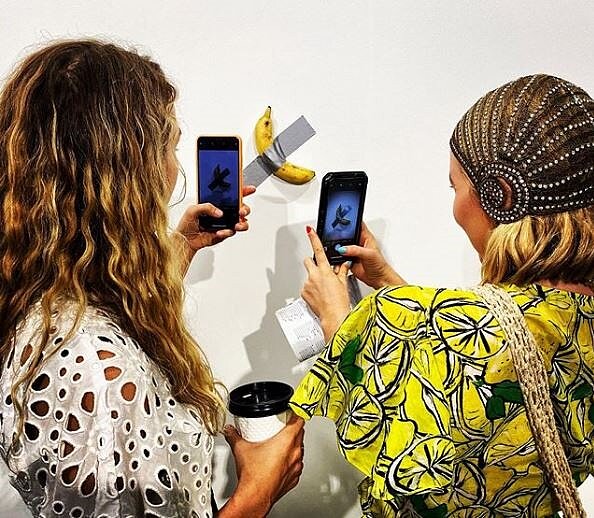 邁阿密巴塞爾藝術博覽會的2名參觀者，用手機拍攝義大利藝術家卡特蘭的作品「丑角」。圖／截取自Instagram@Sarah Cascone