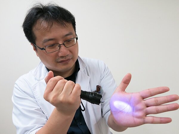 醫師錄製影片分享,鏡頭前利用「螢光液」模擬民眾打噴嚏,將手上的水珠擦拭後,手上雖然沒有髒污或水漬,但螢光燈照射下,明顯看見螢光液布滿整隻手掌。圖/豐原醫院提供