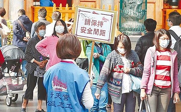 為防制新冠疫情,行天宮志工手舉告示牌提醒參拜民眾保持安全社交距離。(中時電子報系資料照片)