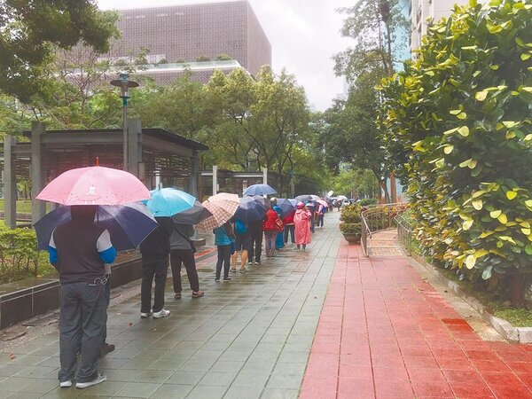 台北市推出口罩販賣機，12日為試辦第一天，現場許多民眾都冒雨排隊購買。（張薷攝）