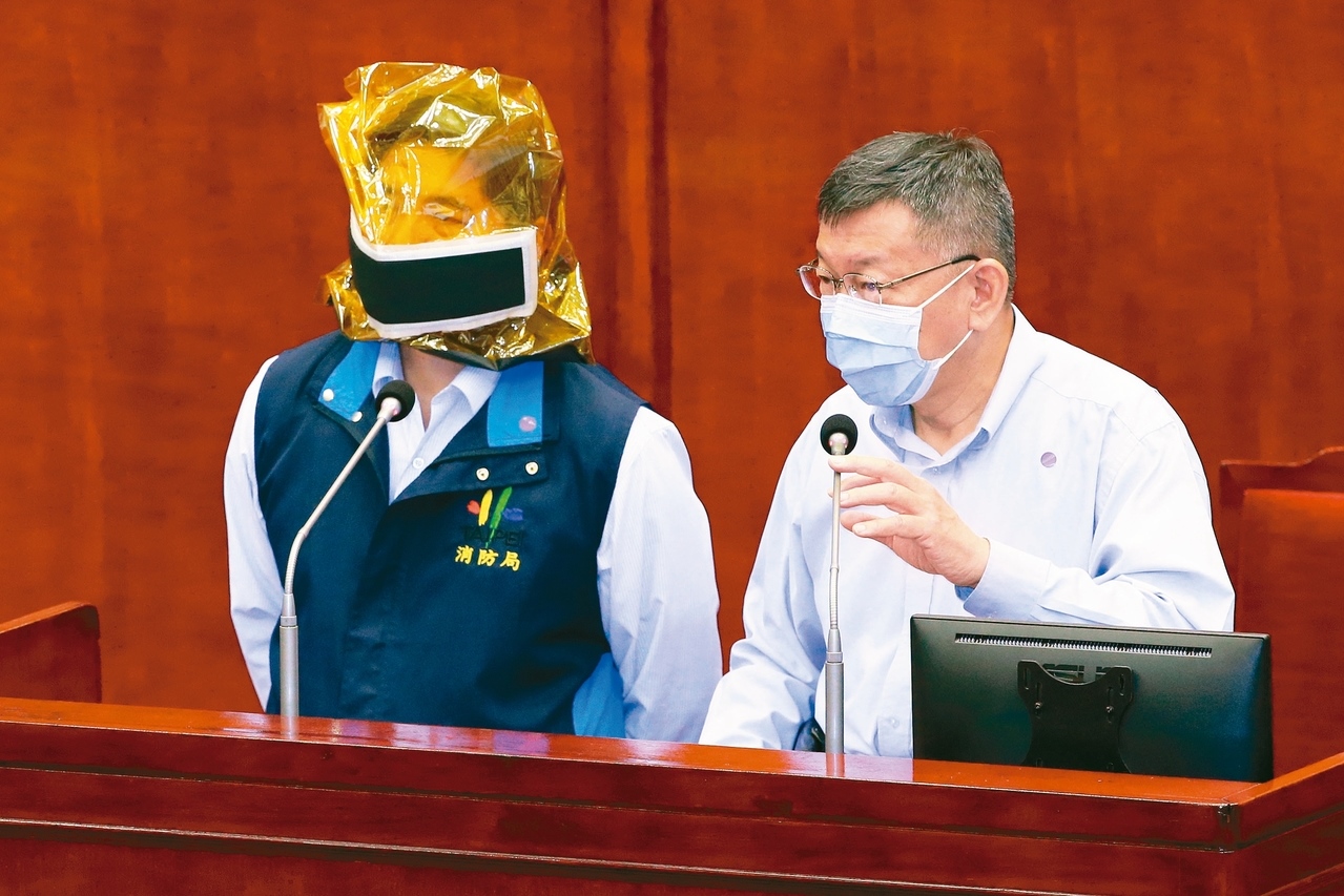 台北市長柯文哲（右）昨赴議會進行錢櫃大火報告，議員質詢時拿防煙面罩給消防局長吳俊鴻（左）試戴，要求北市營業場所全面設置。 記者許正宏／攝影