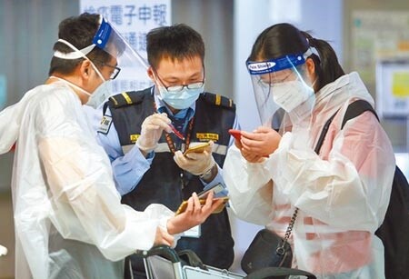 中央流行疫情指揮中心研擬開放「經濟泡泡」,放寬特定身分旅客入境檢疫條件。在桃園機場入境管制區內,防疫人員正協助2名身穿防護衣的旅客,上網填寫健康聲明書。(范揚光攝)