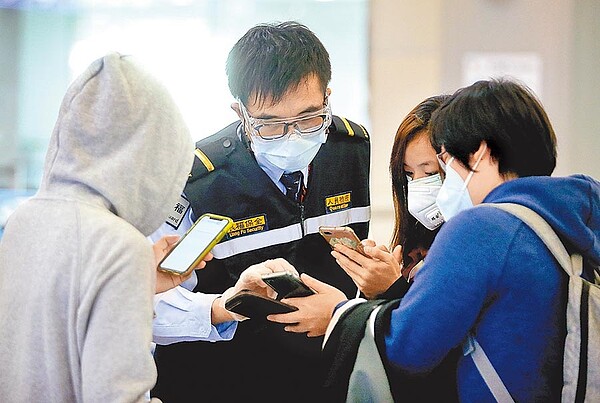 在桃園機場入境管制區內，1名防疫人員正協助入境旅客，上網填寫健康聲明書。（范揚光攝）