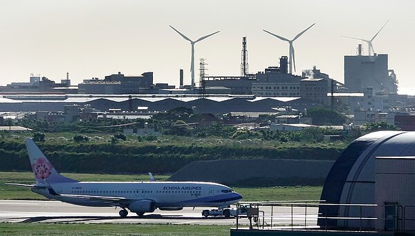 桃園觀音外海將蓋離岸風機,可會導致桃機第三跑道蓋不成,圖為桃園機場北跑道上被拖行的航機,遠方是現有的台電風機。記者鄭超文/攝影