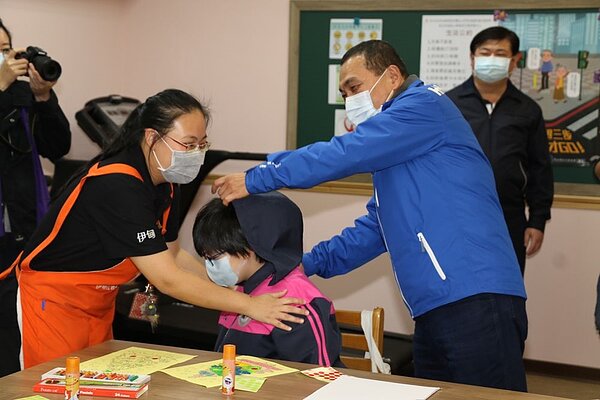 侯友宜在幸福日照中心幫一位上課的學員親切的拉上外套帽子。圖／新北市政府提供