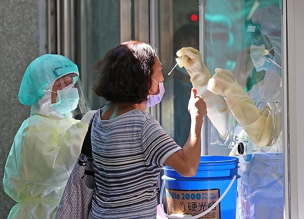 新冠肺炎嚴峻,新北市中和在市民活動中心設置社區篩檢站,醫護人員隔著玻璃逐一採檢,受檢民眾豎起拇指稱讚謝謝醫護人員的幫忙。 記者潘俊宏/攝影