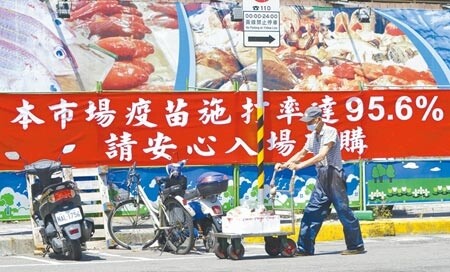 台北市連續爆發群聚感染，萬大市場部分攤位24日晚間突然停業消毒，並已封鎖近14天可能有接觸確診者的36個攤位，27日市場周邊購買人潮銳減，苦不堪言，圖為一位攤商推車經過宣導布條。（陳俊吉攝）