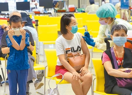 第8輪AZ疫苗持續施打，民眾20日至台北市花博站接種，一位小朋友緊盯著手機，完全忽視一旁正在接種的家長。圖／記者陳君瑋攝影