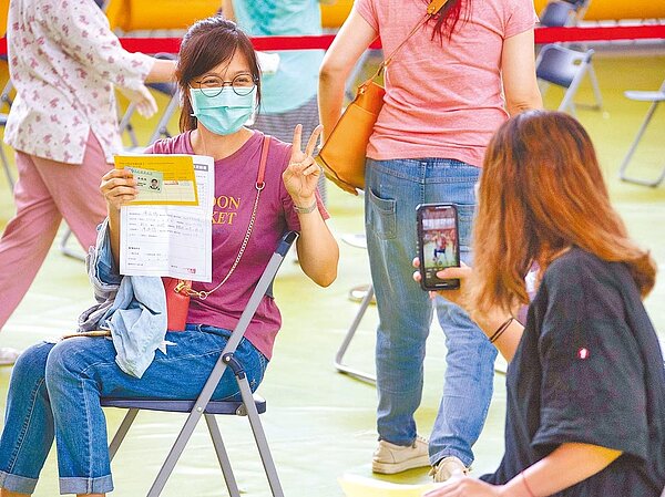 因應暑假後要開學，新北公私立國小教職員已陸續分流接種，聯合醫院21日在大觀國中設立接種站。一名教職員施打疫苗前，不忘請同事幫忙拍照，紀念難得的一刻。(羅永銘攝）