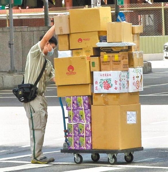 近年網購大增,網購包裝減量成效欠佳。圖為快遞人員拉著堆著滿滿貨品的手推車小心過馬路。(本報資料照片)