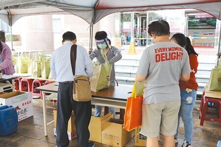 桃園市中壢區公所工作人員與代領民眾確認資料與防疫包內容物。（蔡明攝）