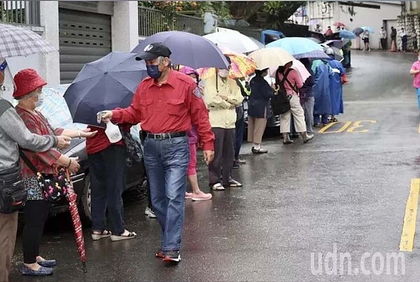 台北松山慈惠堂向民眾免費發放快篩試劑。民眾撐著傘、穿雨衣一路從山上慈惠堂的廣場，排到山下的福德路的路口，工作人員幫忙排隊民眾噴酒精消毒。記者黃義書／攝影