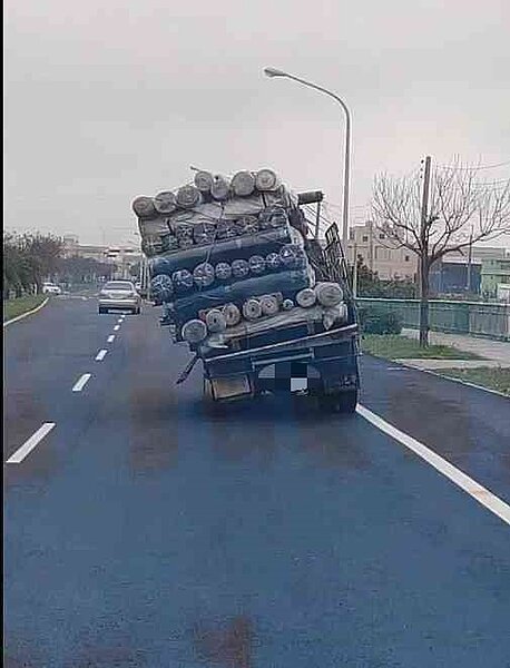 彰化縣美港公路伸港段今天上午10點出現一輛貨車載著布匹,但疑似位捆綁好,整個歪斜,從後方看起來就像「移動的布匹斜塔」。圖/翻攝彰化踢爆網