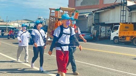 台東市劉部堂堂主陳致廷(著紅褲者)獨自背著神像,在少數信眾的陪伴下,徒步走在街頭,前往民眾家祈福。(蔡旻妤攝)