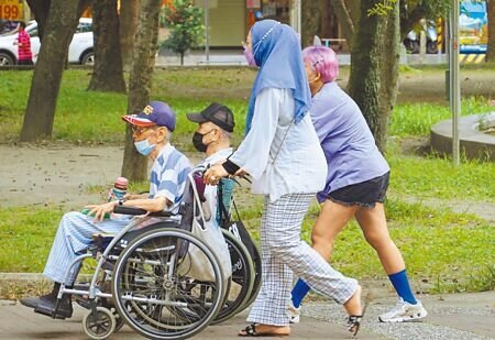 勞動部宣布自10日起,新招募或期滿續轉聘的家事移工適用調薪新制,每月薪資由1.7萬元調高至2萬元。圖為傍晚時分,外籍看護推著坐輪椅的長者到公園透氣。(姚志平攝)
