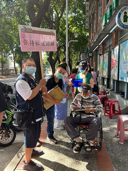 劉泓麟舉牌提醒里民排隊打新冠疫苗也要保持社交距離 圖片由劉泓麟里長提供