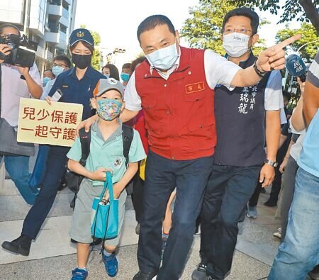 新北市長侯友宜(中)30日前往光復國小關心開學防疫落實情形,並護送小學生過馬路進校門。(劉宗龍攝)