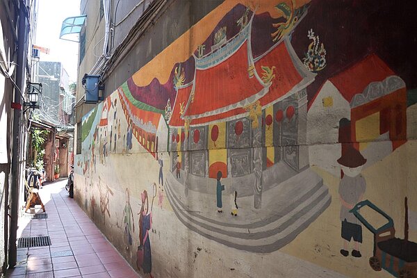 米市巷入口右方的牆面彩繪是由新泰國小師生所畫，牆上描繪過往熱鬧的廟街景象。圖／林昕璿攝