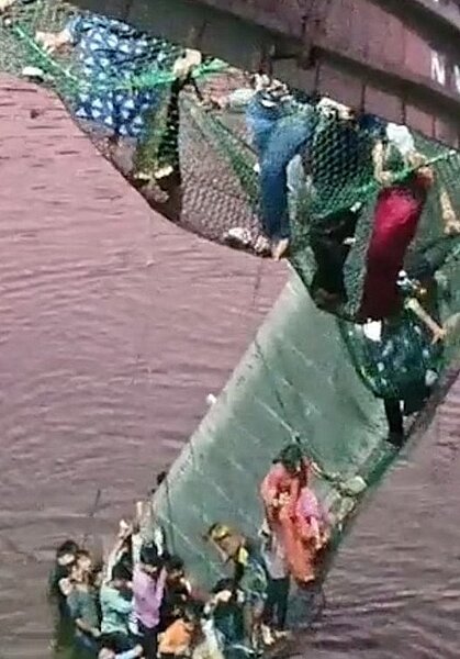 印度西部古茶拉底省一座吊橋30日突然斷落。圖中可見民眾拚命抓著橋上支撐物,等待營救。圖/取自推特