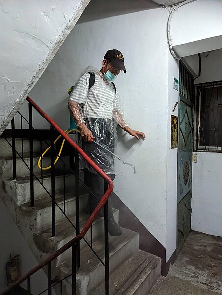 里長林錫祺在樓梯間替里民消毒 。圖／由忠貞里里長提供