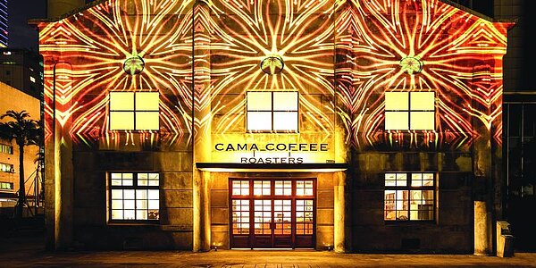 cama cafe’在台北松山文創園區開設第二家旗艦店「CAMA COFFEE ROASTERS 豆留文青」,入夜後新店外牆有光雕投影,使古蹟建築華麗變身。圖/cama cafe’
