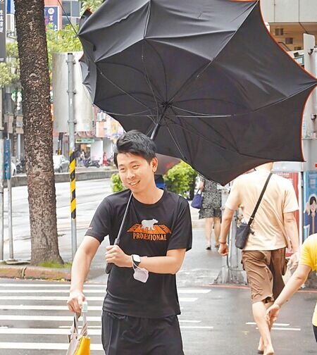 
卡努颱風來襲，3日白天雨勢不大，但風勢忽強忽弱，街頭民眾的大傘遭強風吹翻。（姚志平攝）
