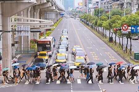 在新北市新莊區思源路、幸福路口，民眾穿黑衣、右手撐傘、左手持康乃馨、左肘套上繃帶，繞行路口呼籲還路於民，終結行人地獄的惡名。（黃世麒攝）
