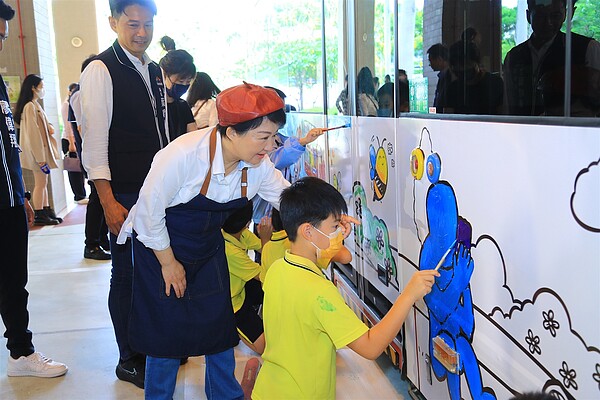 盧秀燕頭戴畫家帽手拿畫筆,帶領黎明國小學童一起將公車線稿填上五彩顏料。圖/台中市交通局提供