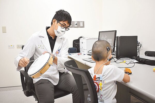 健保署昨宣布放寬人工電子耳適用條件,從過去限單側植入,改為雙側植入。圖為聽力師敲打樂器以觀察完成人工電子耳手術並開頻的幼童開頻後的反應。(新竹台大生醫醫院提供/羅浚濱新竹傳真)