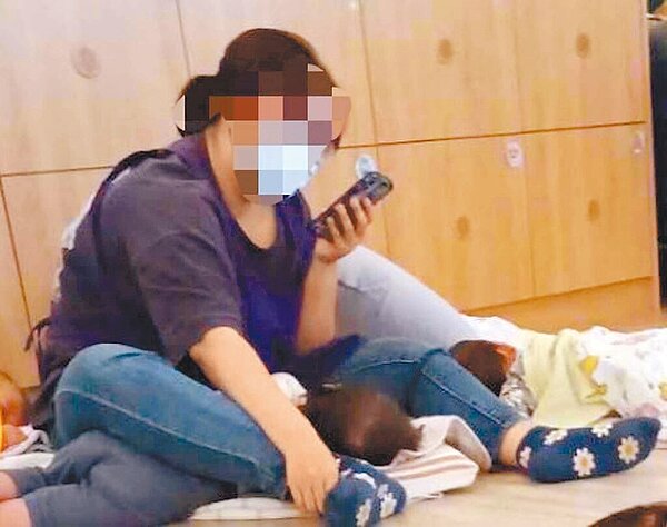 高市右昌公共托嬰中心去年開幕,但營運不到1年竟爆出多起不當管教事件,日前有老師用腳強壓孩子,全神灌注看手機。(高市議員白喬茵提供/柯宗緯高雄傳真)