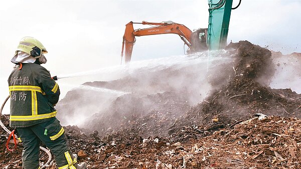 新竹縣新豐鄉垃圾掩埋場15日下午又自燃，竄出大量惡臭濃煙，消防員出動2輛挖土機開挖，試圖排除底層悶燒。圖／新竹縣消防局提供
